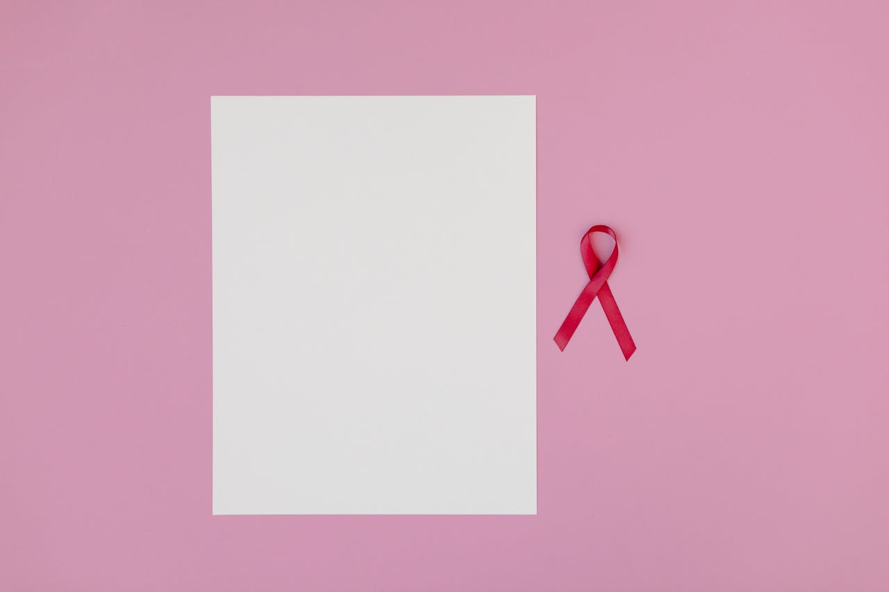 Pink background with a blank paper and a red ribbon symbolizing breast cancer awareness.