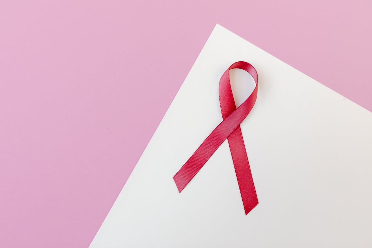 Close-up of a pink awareness ribbon on a white paper with a pink background, symbolizing breast cancer awareness.